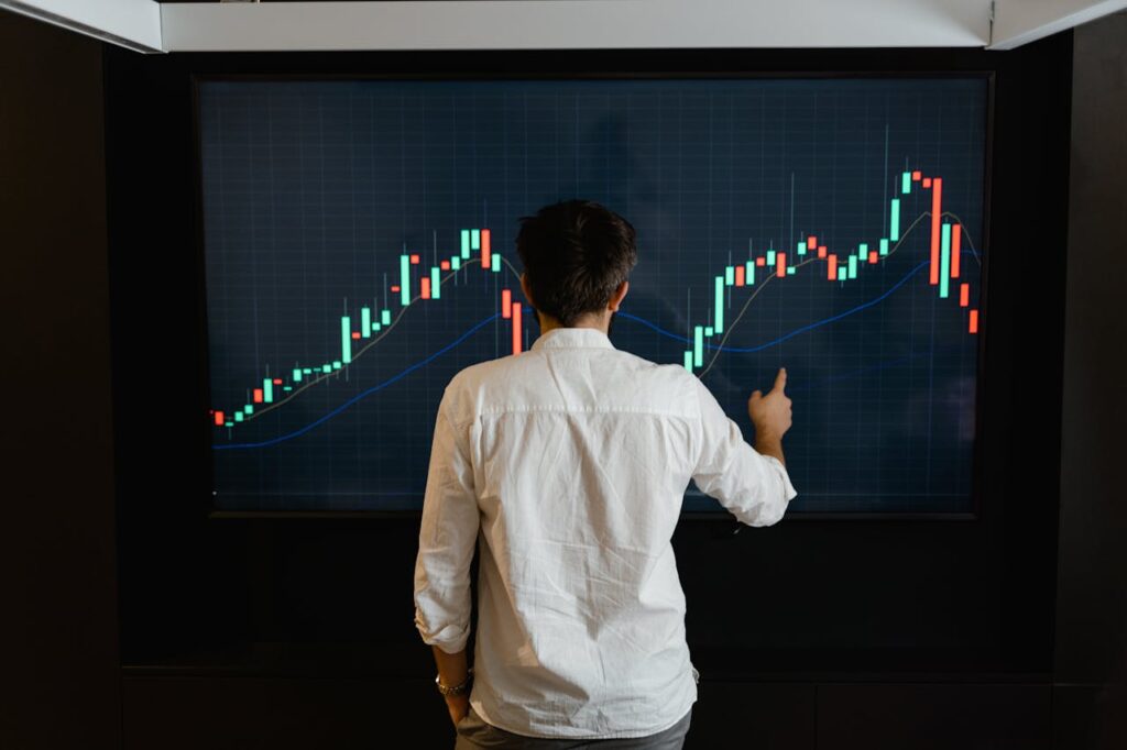 Adult male reviewing stock market data on a large display screen indoors.