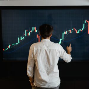 Adult male reviewing stock market data on a large display screen indoors.