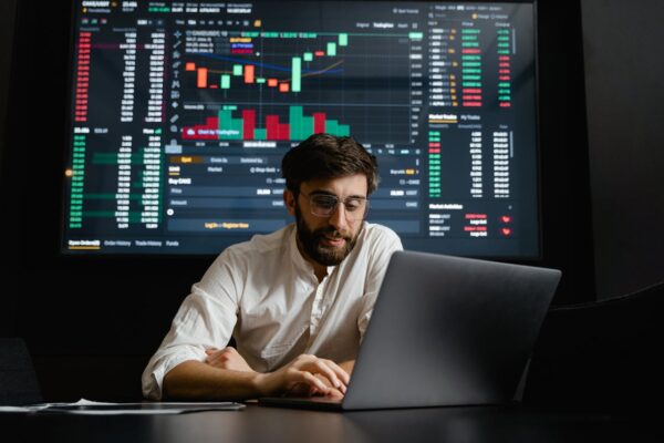 Male analyst studies cryptocurrency trends at a workstation with multiple displays showing market data.